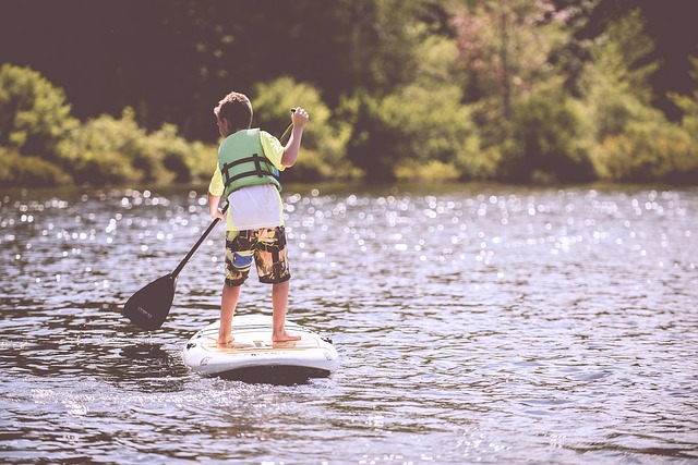 boy with life jacket paddle boarding on lake