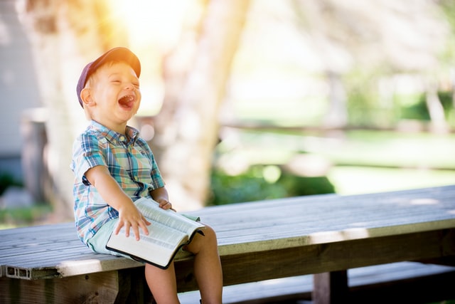 boy wearing hat laughing while holding Bible